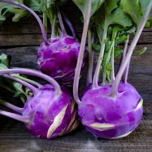 Fresh purple kohl rabi vegetables with green leaves on rustic wooden background.